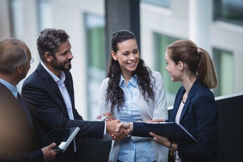 Four people shaking hands in an outdoor setting with modern buildings in the background. 1