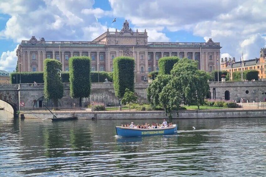 A historic building with a river in front, a boat with people, and well-maintained trees. 4