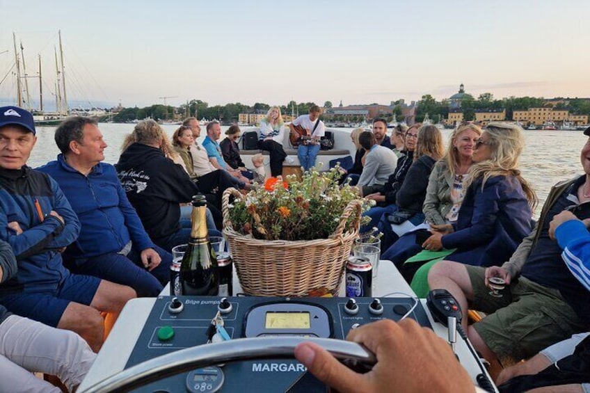 A group of people on a boat with a captain steering, a basket of flowers, and bottles of champagne. 1