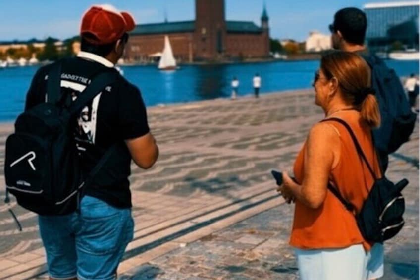 A group of people standing on a waterfront promenade with a sailboat in the background. 2