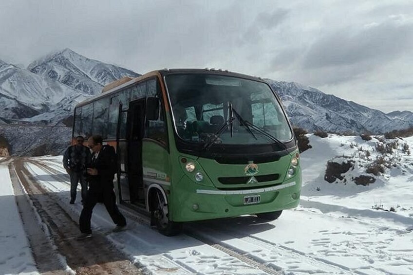 Ein grüner Bus ist auf einer schneebedeckten Straße geparkt, im Hintergrund sind Berge zu sehen. 3
