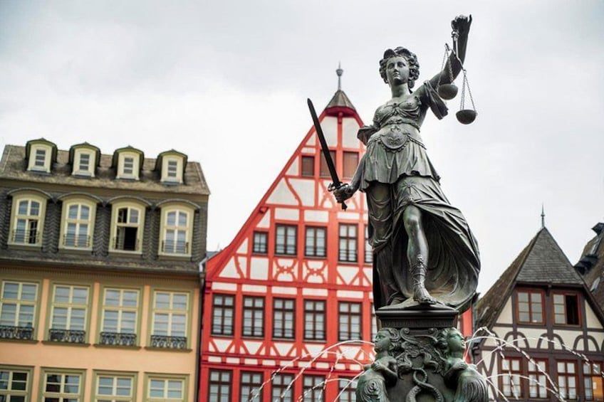 A statue of a woman holding scales and a sword, with colorful buildings in the background. 5