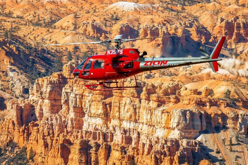 A red helicopter with 'ZION Helicopters' and 'N35 FS' on its side flying over a rocky canyon. 1