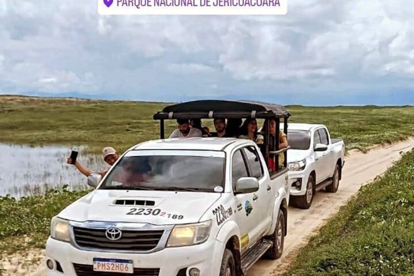 En vit Toyota-pickup på en grusväg, med en vattenyta och gräsbevuxna fält i bakgrunden. 3
