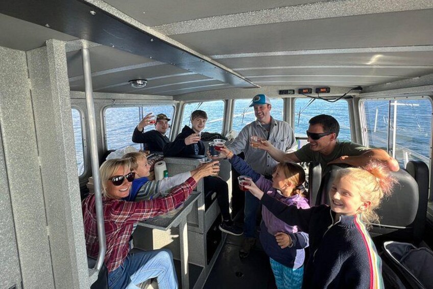 A group of people on a boat, some holding drinks, with a view of the water outside. 3