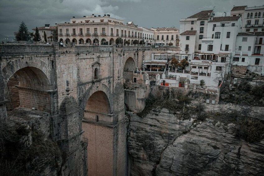 An old stone bridge with arches, a building with a white facade, and a rocky terrain. 3