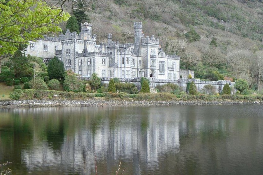A large, historic stone building with multiple towers, surrounded by a body of water and lush greenery. 1