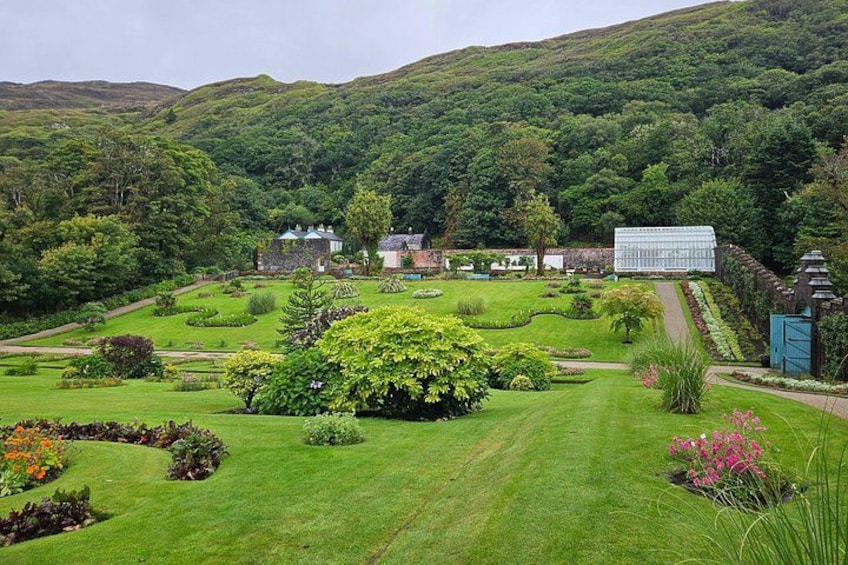 A lush garden with a variety of plants and flowers, a stone wall, and a building in the background. 3