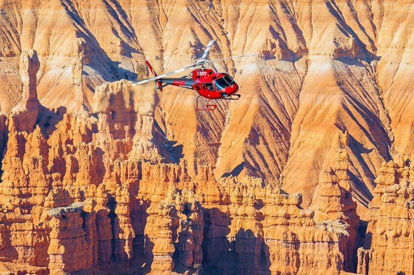 A red helicopter flying over a canyon with rugged, layered rock formations. 5