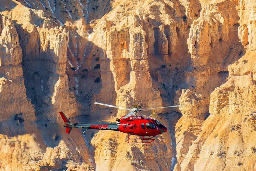 A red helicopter flying over a rocky canyon. 3