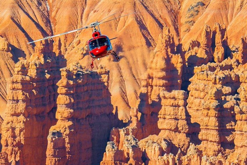 A red helicopter flying over a canyon with layered rock formations. 4
