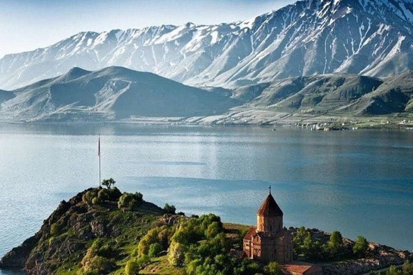 Un lago con una pequeña iglesia en una colina, rodeado de montañas. 2