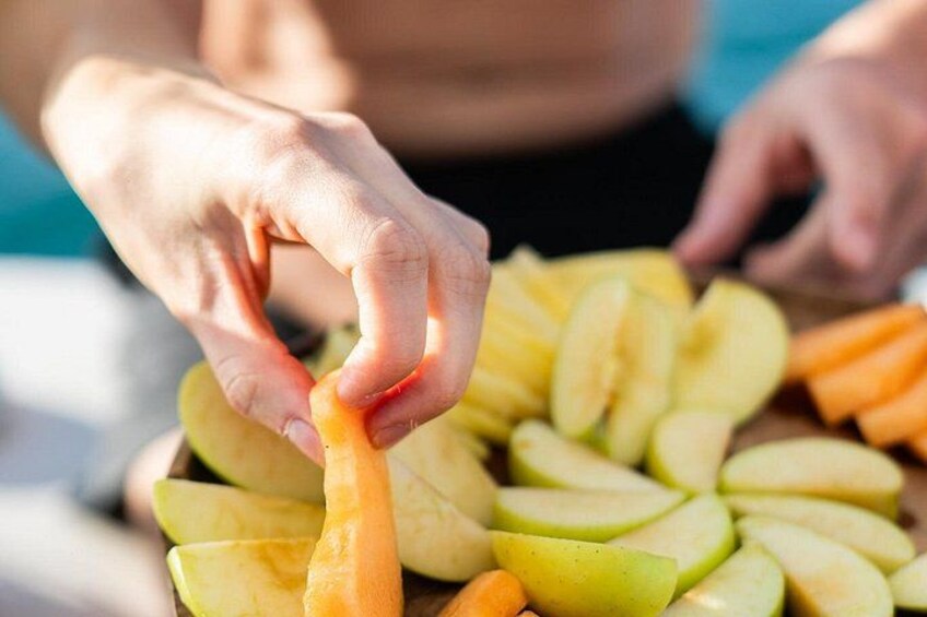 Hands peeling a carrot from a pile of sliced fruits. 2