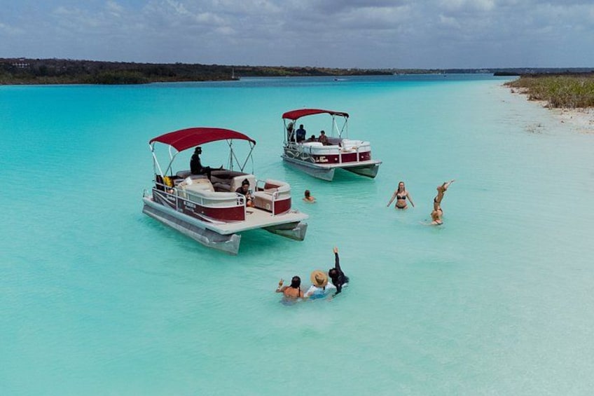 Two boats with red canopies on turquoise water, people swimming and sunbathing on the shore. 5