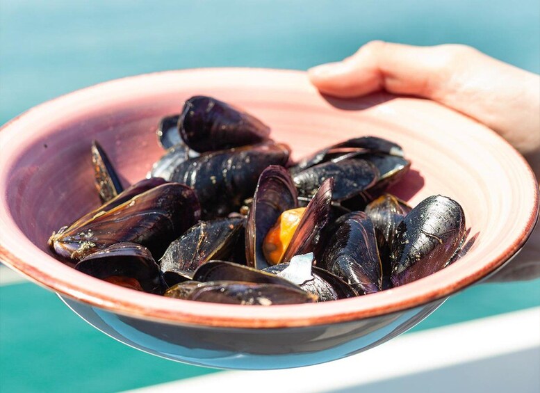 A bowl of mussels with a hand holding it. 3