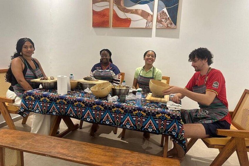 Vier personen zitten aan een tafel met een tafelkleed met patroon, kommen en een fles. 3