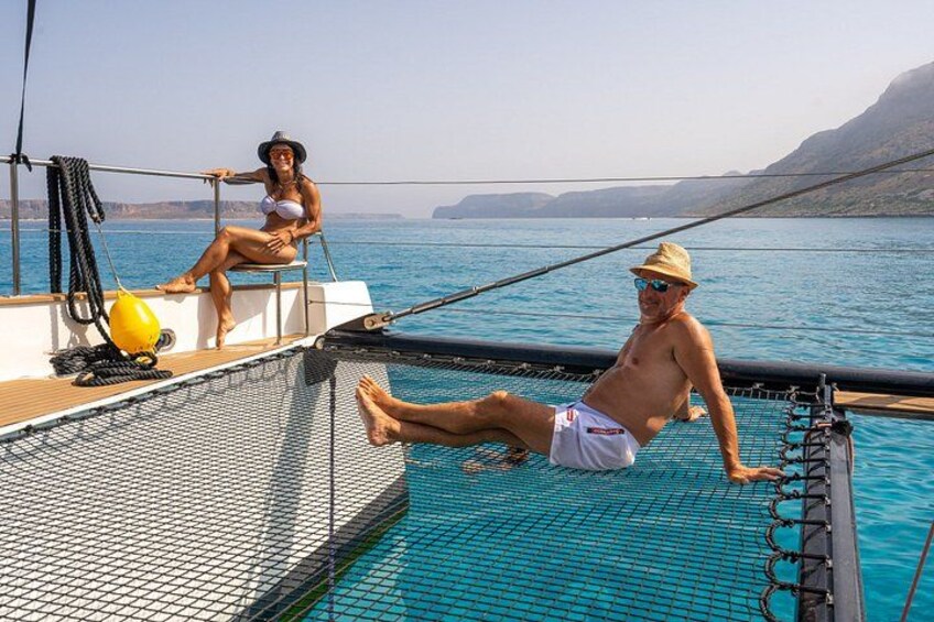 Une personne se trouve sur un bateau, une autre est assise au bord du bateau, et une mer bleue et limpide s’étend devant eux, avec une terre lointaine visible à l’horizon. 4