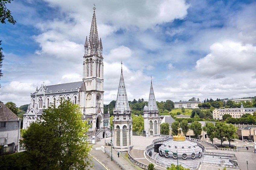 A cathedral with two spires, a circular plaza with a fountain, and surrounding buildings. 3