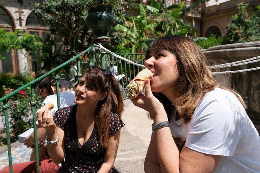 Twee vrouwen zitten op de trap, waarvan er één een gebakje eet. 4