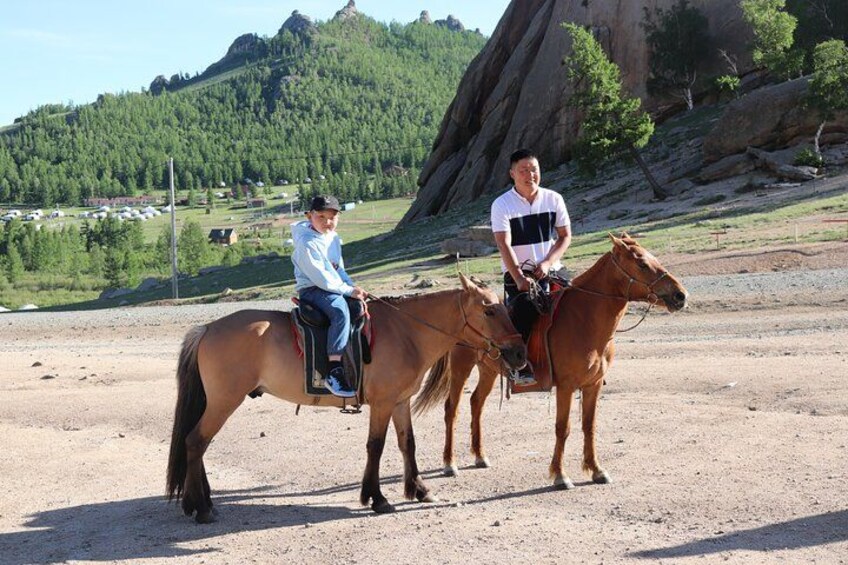 Two people riding horses on a dirt path with a mountainous landscape in the background. 5