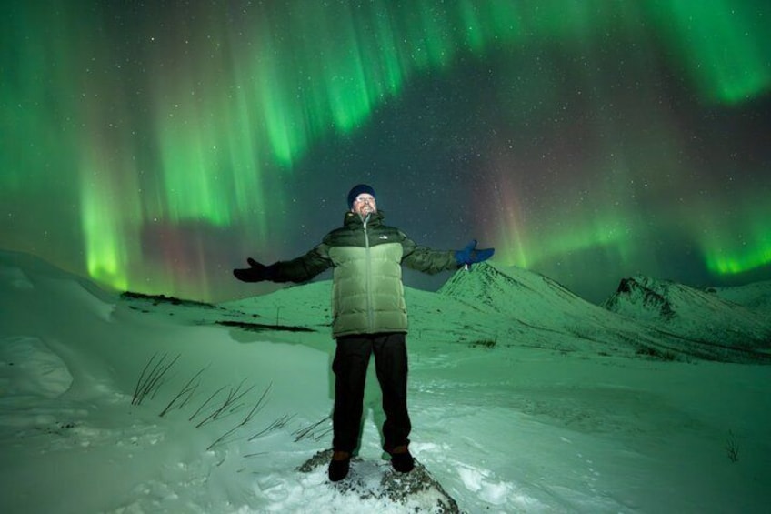 A person standing on snow with arms outstretched, facing the northern lights. 3