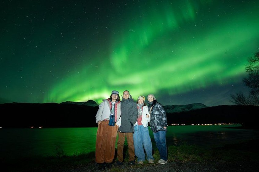 A group of people standing by a lake with the aurora borealis in the background. 3
