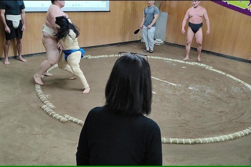 Un combate de sumo con dos luchadores con atuendo tradicional, un árbitro y un público. 3