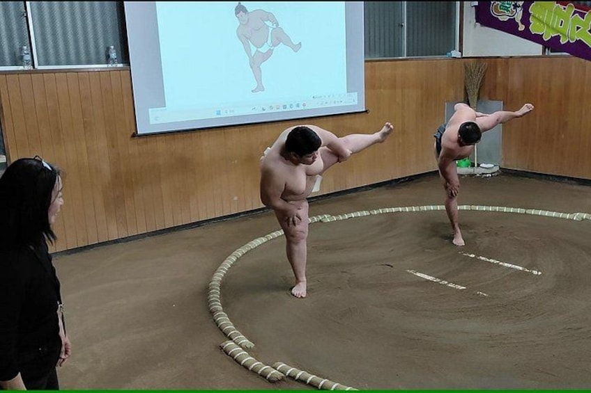 Dos hombres practicando artes marciales en una habitación con una pantalla de proyector mostrando una figura. 5