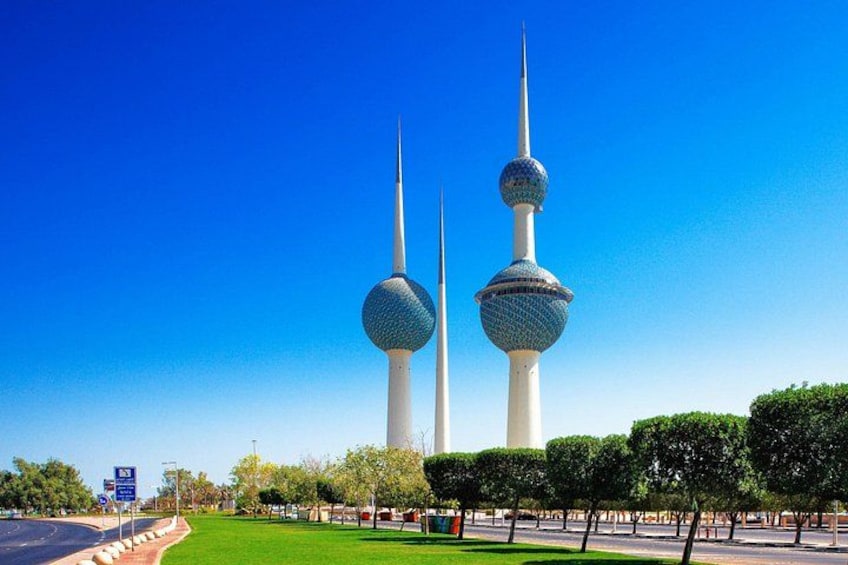 Two tall towers with spherical tops, a clear blue sky, and a well-maintained park with trimmed trees. 1