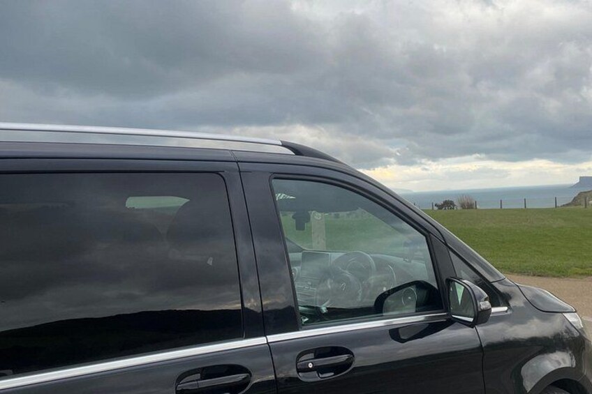 Una furgoneta negra estacionada en una carretera con un campo cubierto de hierba y un cielo nublado al fondo. 2