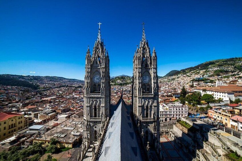 A cathedral with two tall towers and a clock, surrounded by a cityscape with buildings and hills. 3