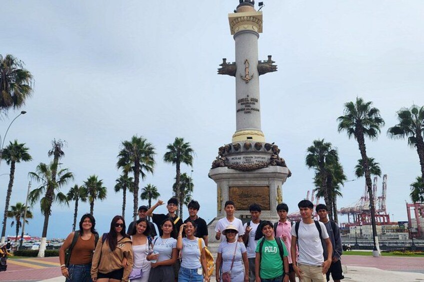 A group of people standing in front of a tall monument with a clock, palm trees, and a clear sky. 4