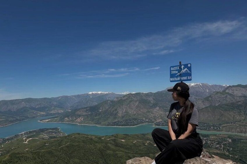 Una persona sentada sobre una roca, con un paisaje montañoso y un lago al fondo. 3