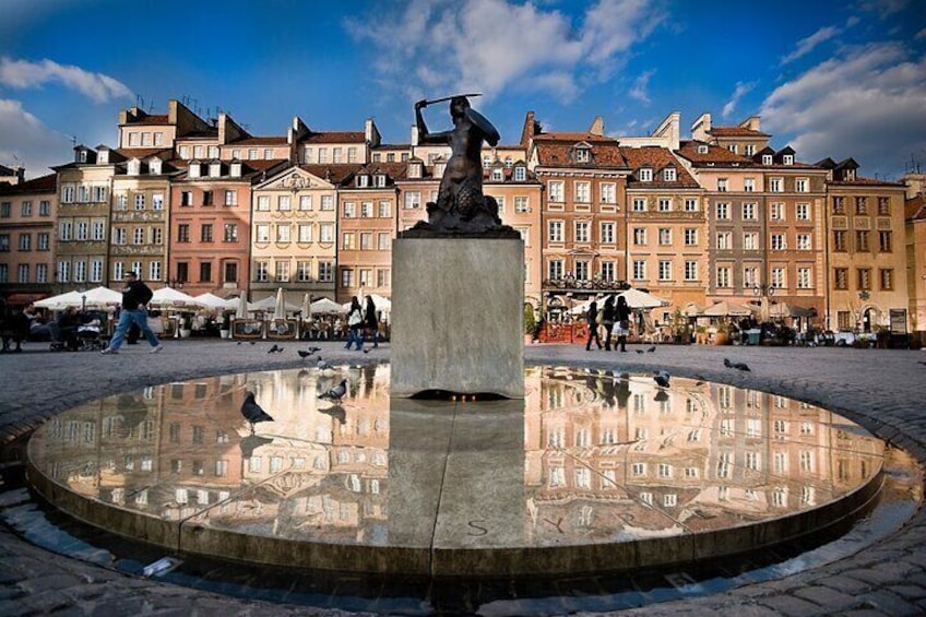 En rund fontän med en staty i mitten, omgiven av ett torg med byggnader i bakgrunden. 2