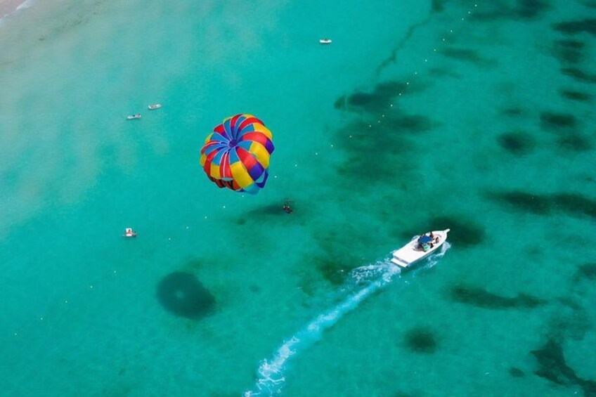 Een parasail boven turquoise water, een boot en iemand die parasails. 3