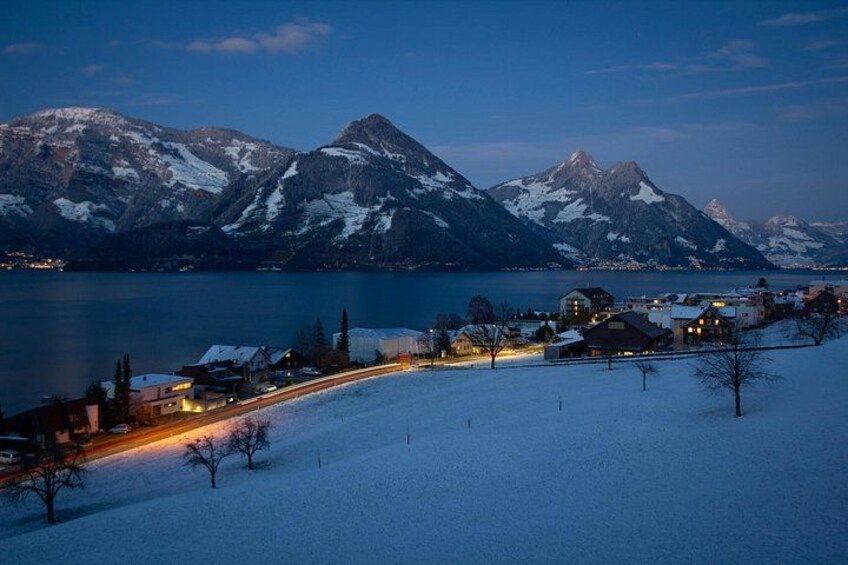 A snow-covered landscape with a lake, mountains, and a small town with houses and lights. 3