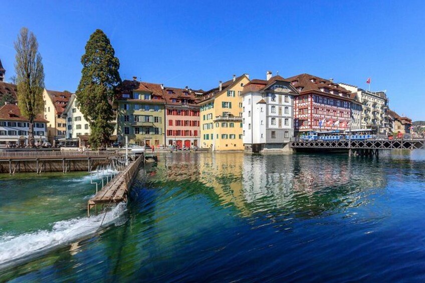 A river with buildings reflecting on the water, a dock, and a clear blue sky. 2