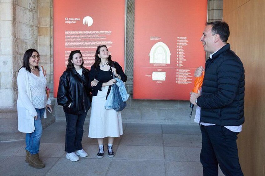 A group of people standing in front of a red informational sign, with a man holding a microphone. 2