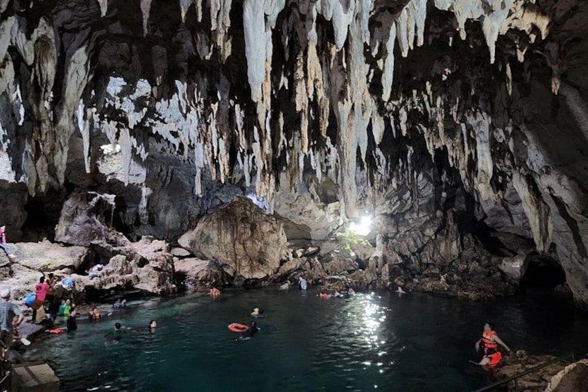 A cave with stalactites and stalagmites, a pool of water, and people swimming and standing around. 4