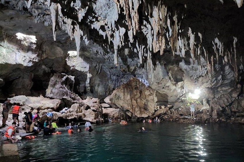 A cave with stalactites, water, and people swimming. 3