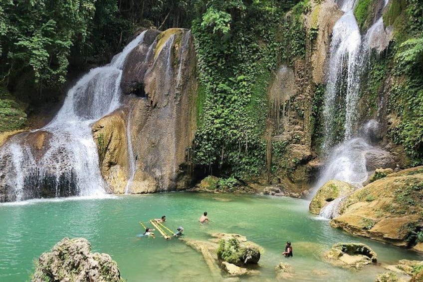 A waterfall, clear water, and people swimming. 2