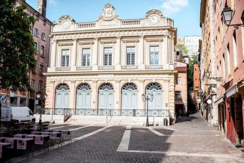 Ein historisches Gebäude mit Bogenfenstern und einer Uhr, eine gepflasterte Straße und ein weißer Transporter vor der Fassade. 5