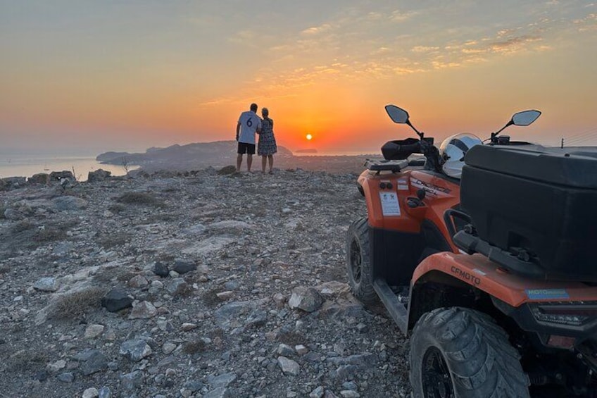 Un paysage rocheux, avec un coucher de soleil en arrière-plan, un quad et deux personnes debout. 1