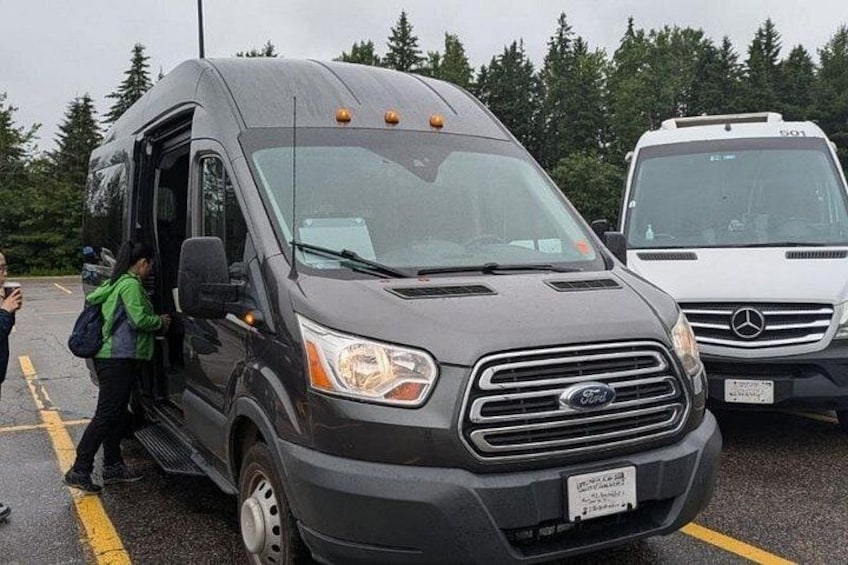 A black Ford van with a person exiting, parked in a lot with a white van in the background. 3