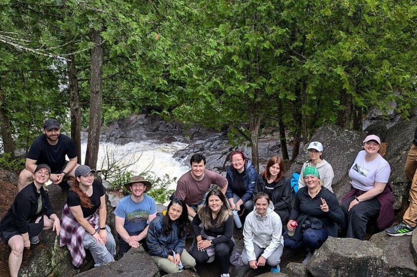 A group of people sitting on rocks near a waterfall in a forested area. 1