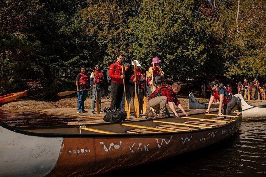 People preparing canoes on a dock by a forested river. 2