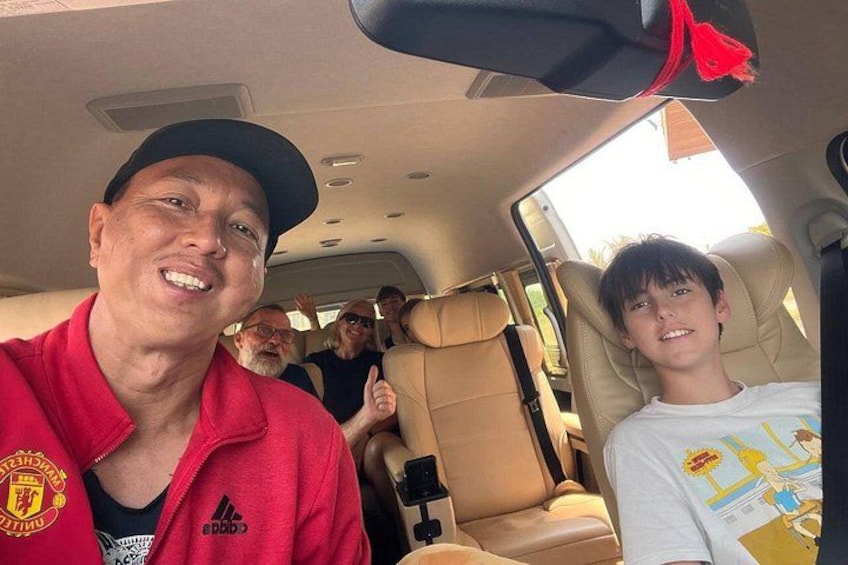 A car interior with beige leather seats, a red seatbelt, and a child in a white shirt. 1