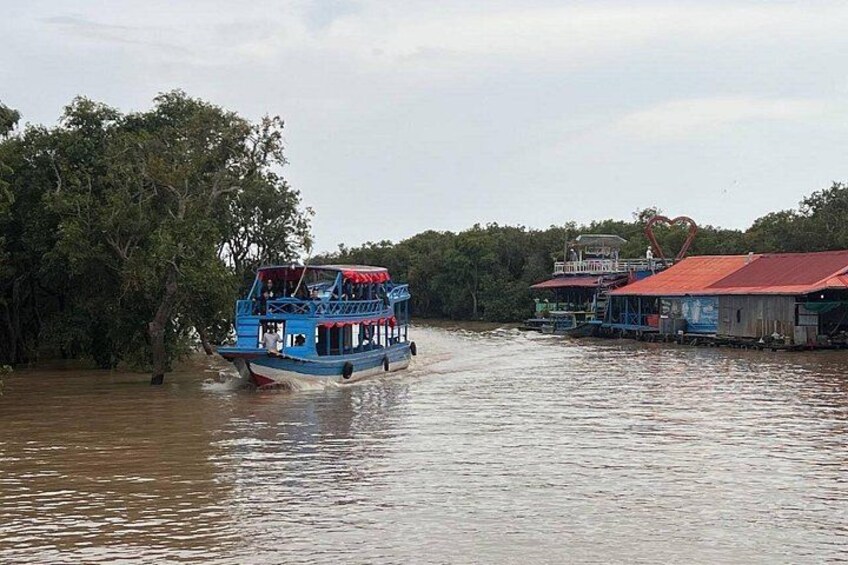 A blue boat with a red roof on the water, surrounded by trees and a building with a red roof. 5