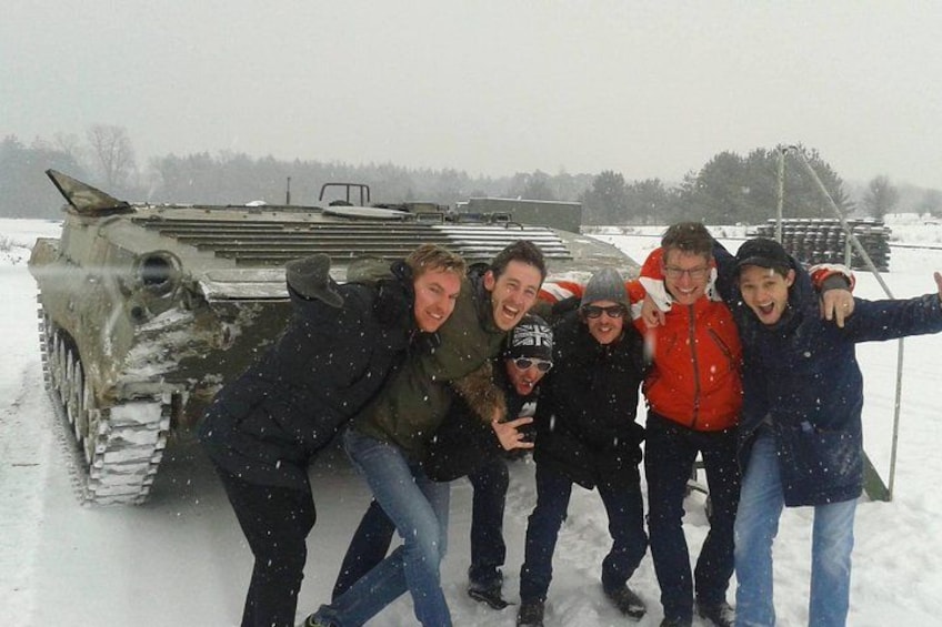 A group of people posing in front of a military tank on a snowy field. 3