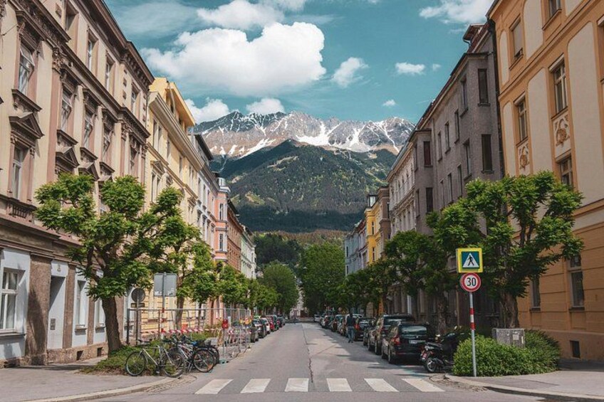 Une rue bordée de voitures garées, de vélos et d’immeubles, avec une montagne en arrière-plan. 3